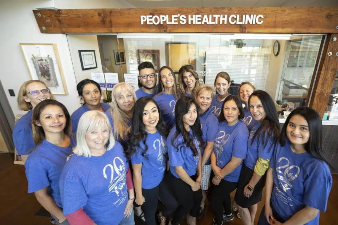 group of people smiling in front of people's health clinic