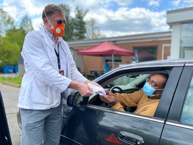 man handing out masks to guy in car